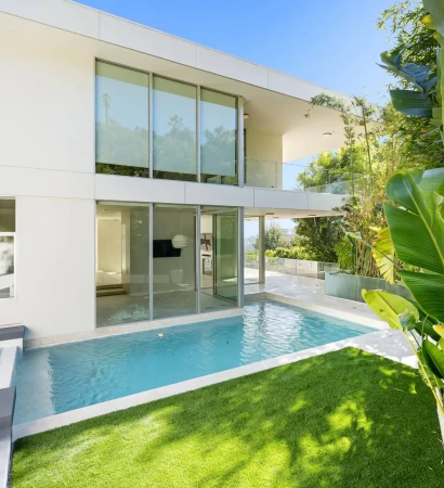 A small pool beside a luxurious white modern house surrounded by plants